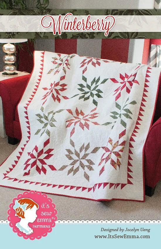 A quilted throw blanket with a white base and red, green, and brown floral/starburst motifs draped over a red armchair. The image includes a decorative banner reading 'Winterberry' and branding for It's Sew Emma Patterns.
Photo by It's Sew Emma [image_link]
