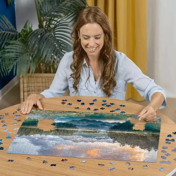 Woman working on a puzzle of a beach scene at a table.
Photo by Ravensburger [additional_image_link]