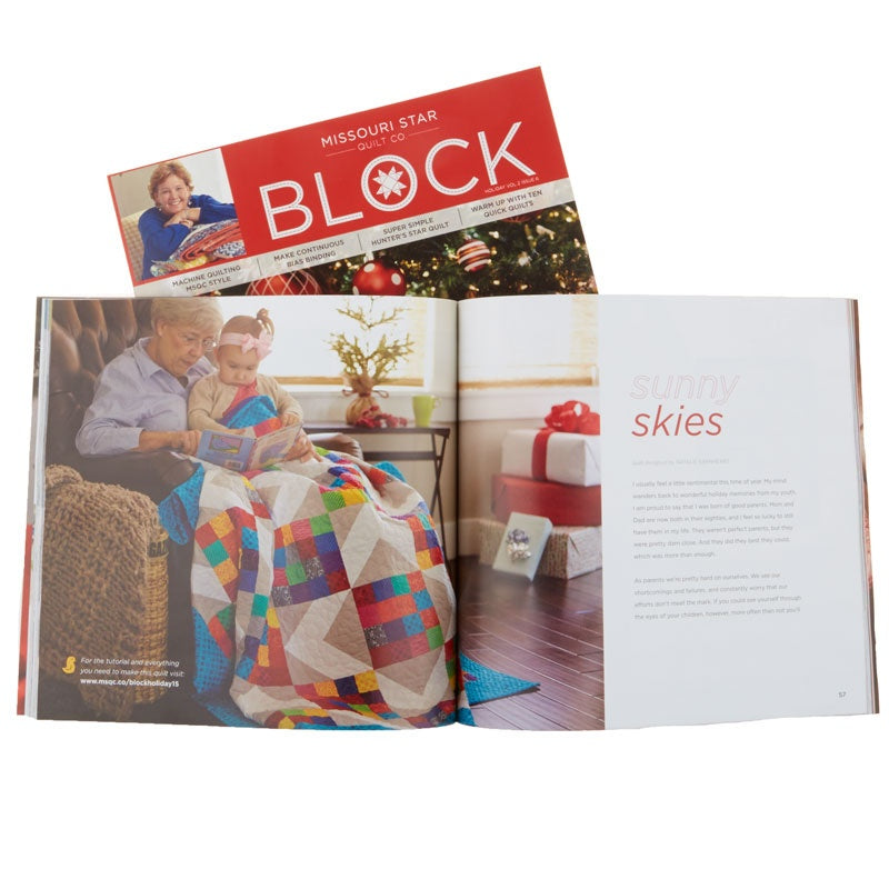 An open magazine or book spread with a red cover page reading 'MISSOURI STAR BLOCK' and a large photo of a man and child reading a colorful quilted blanket, shown against a white background.
[additional_image_link]