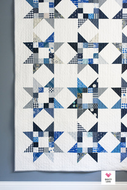 A quilted fabric panel featuring a repeating geometric starburst pattern in shades of blue, navy, gray, and white, with a visible 'Dusty Love' brand label in the bottom right corner.
Photo by Quilty Love [additional_image_link]