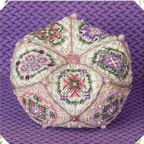 A decorative, hand-embroidered and beaded biscornu shown on a textured purple background.
Photo by JustNan.com [additional_image_link]