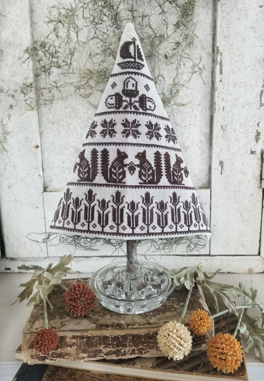 Cross stitch kit ornament in progress, depicting a tree with autumn-colored leaves, displayed on a linen background with its pattern and floss visible.
Photo by HelloFromLizMathews.com [image_link]