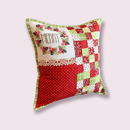 A square Christmas-themed patchwork throw pillow with a green and red border, featuring a white embroidered 'MERRY' section with floral details, on a light pink background.
Photo by HandsOnDesign.biz [additional_image_link]