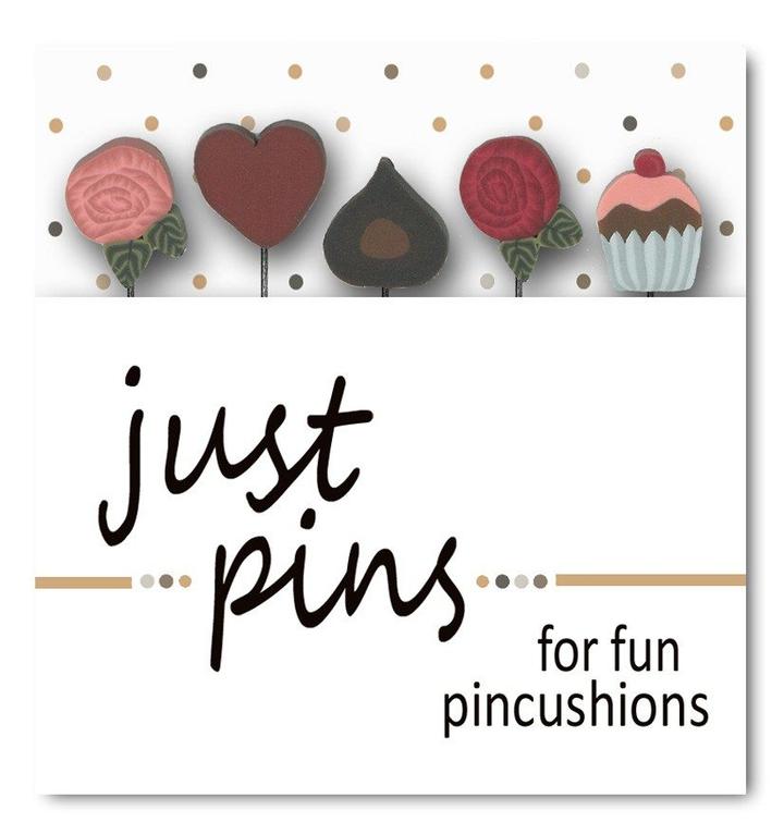 Packaging for 'Just Pins' pincushion kit, featuring a pink felted wool ball, wooden spool, and pink silk ribbon, with polymer clay pin tops illustrated as cupcake, heart, chocolate and roses.
Photo by JustAnotherButtonCompany.com [image_link]