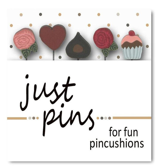 Packaging for 'Just Pins' pincushion kit, featuring a pink felted wool ball, wooden spool, and pink silk ribbon, with polymer clay pin tops illustrated as cupcake, heart, chocolate and roses.
Photo by JustAnotherButtonCompany.com [image_link]