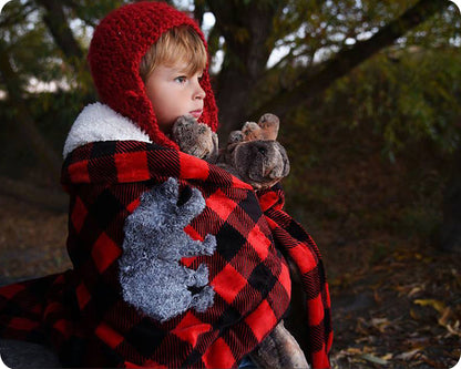 A red and black checkered baby cuddle blanket with a gray bear applique on the bottom right corner, around a toddler sitting outdoors.
Photo by Shannon Fabrics [additional_image_link]