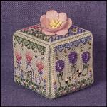 A square decorative box with a floral pattern, featuring a pink flower on top, set against a purple textured background.
Photo by JustNan.com [additional_image_link]