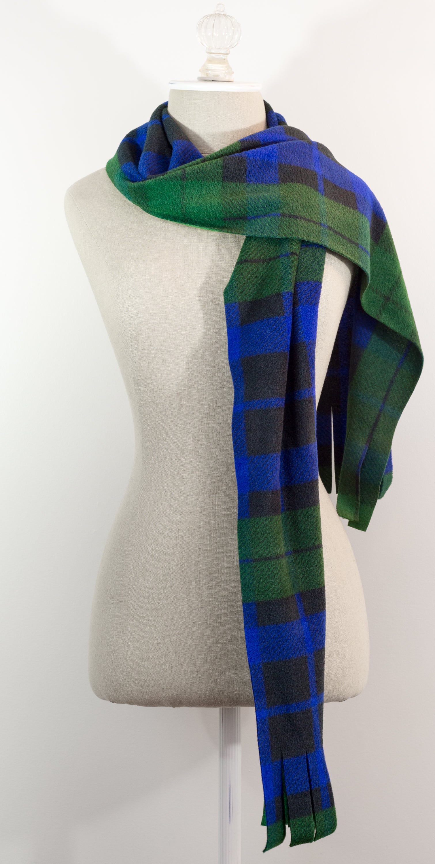 A tartan plaid scarf in green, blue, and black, draped on a white mannequin torso against a white background.
Photo by TheSurgeonsKnots.com [additional_image_link]