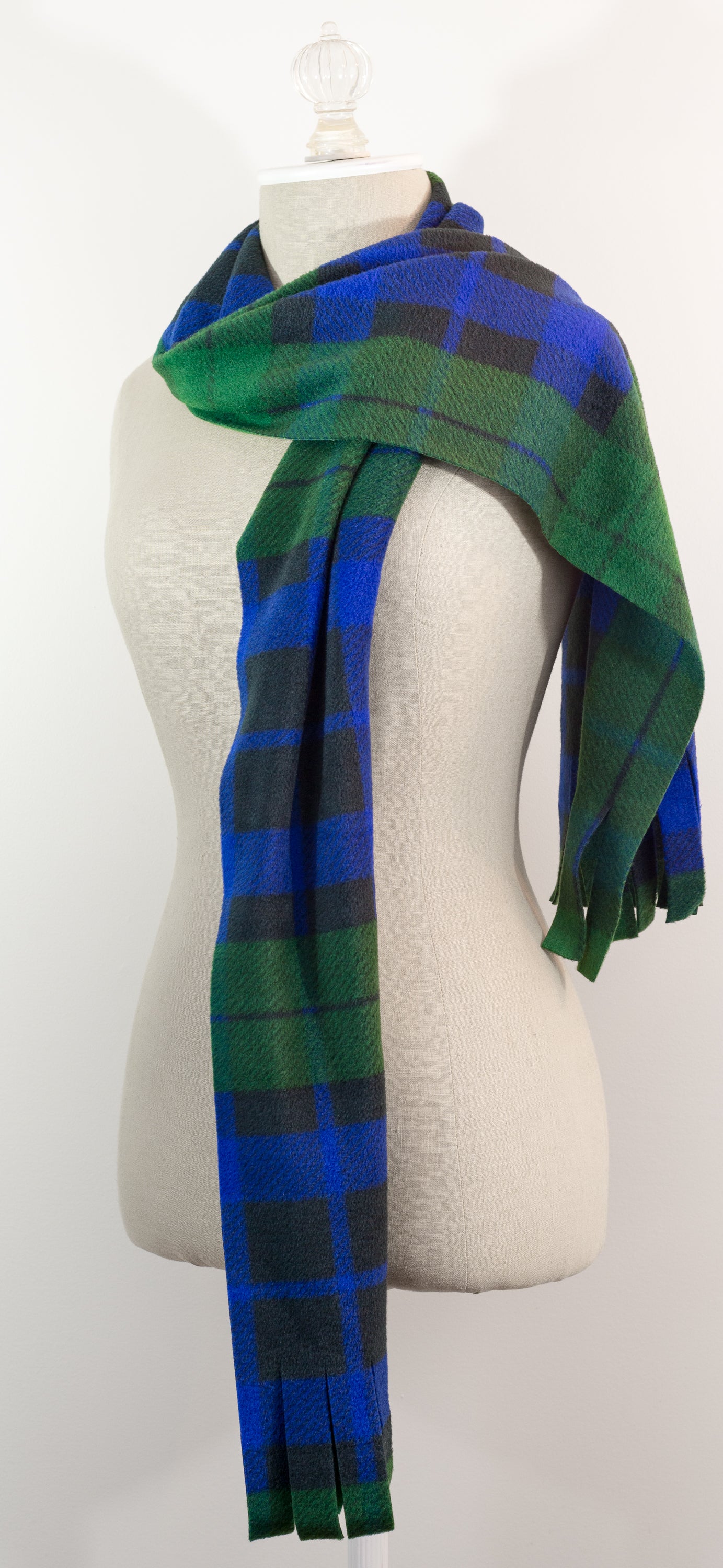 A tartan plaid scarf in green, blue, and black, draped on a white mannequin torso against a white background.
Photo by TheSurgeonsKnots.com [additional_image_link]