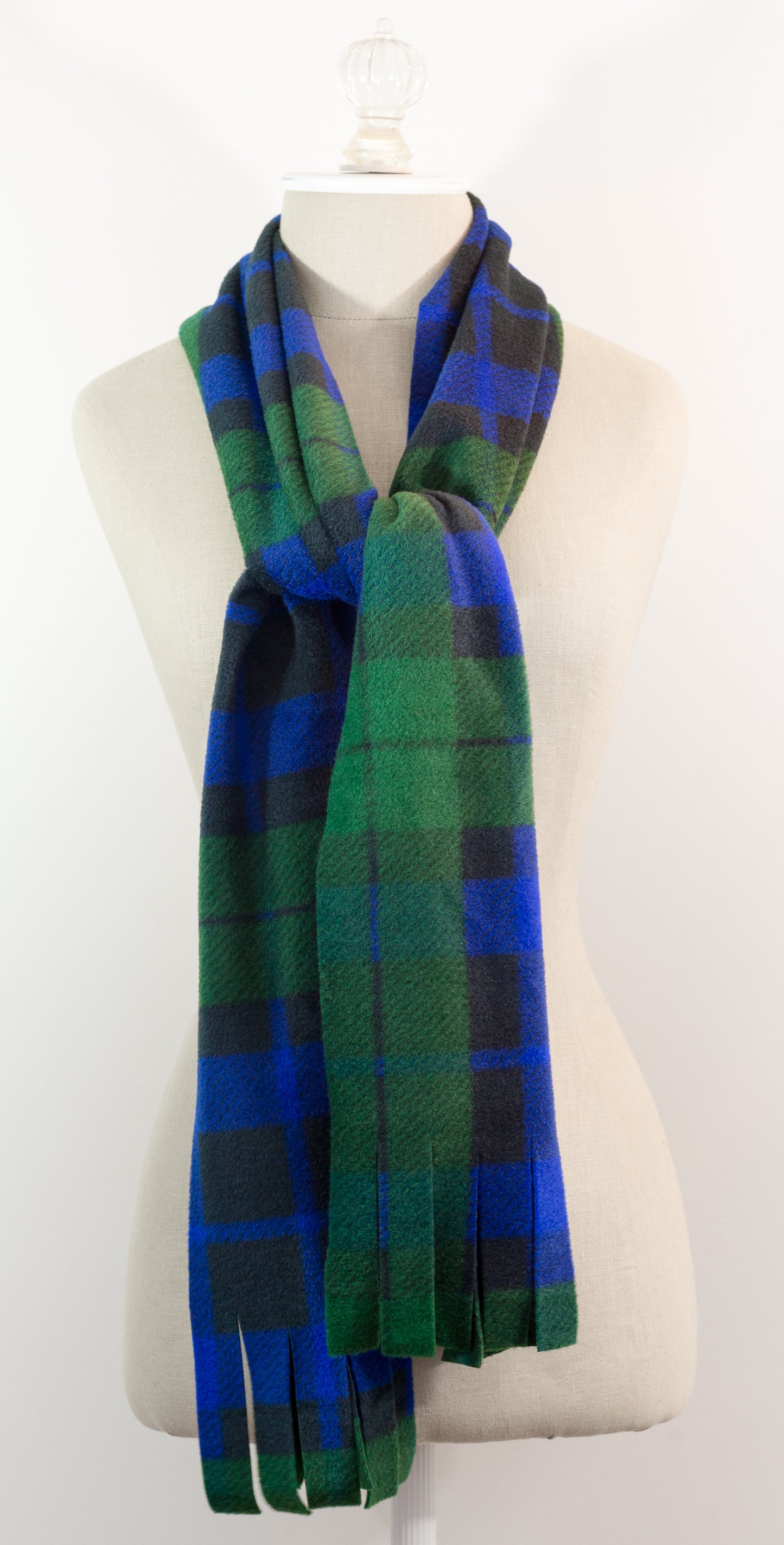 A tartan plaid scarf in green, blue, and black, draped on a white mannequin torso against a white background.
Photo by TheSurgeonsKnots.com [additional_image_link]