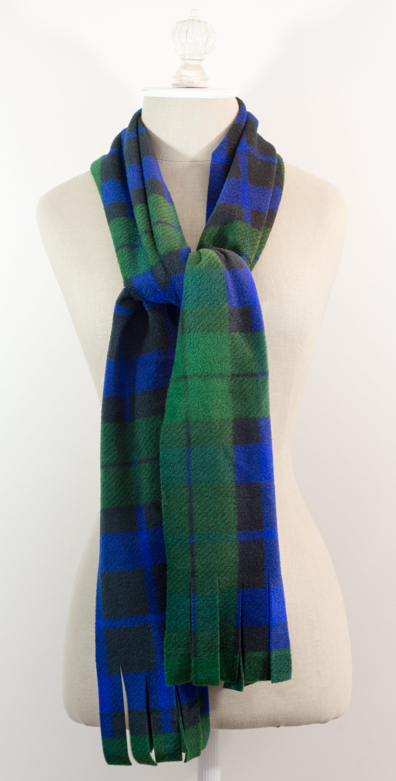 A tartan plaid scarf in green, blue, and black, draped on a white mannequin torso against a white background.
Photo by TheSurgeonsKnots.com [additional_image_link]