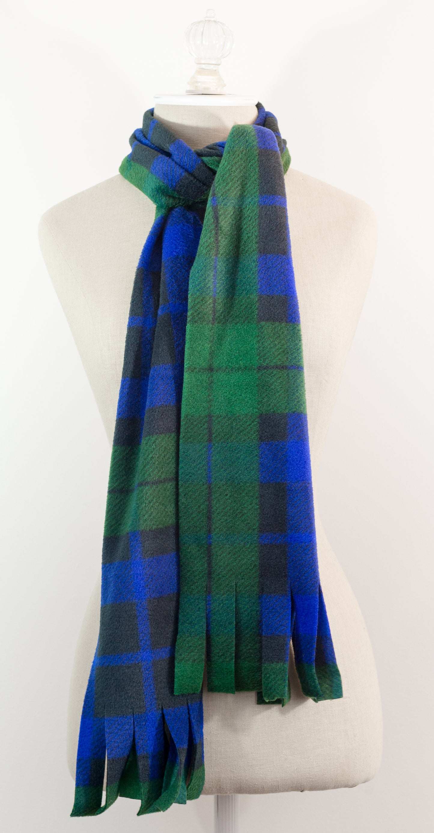 A tartan plaid scarf in green, blue, and black, draped on a white mannequin torso against a white background.
Photo by TheSurgeonsKnots.com [additional_image_link]