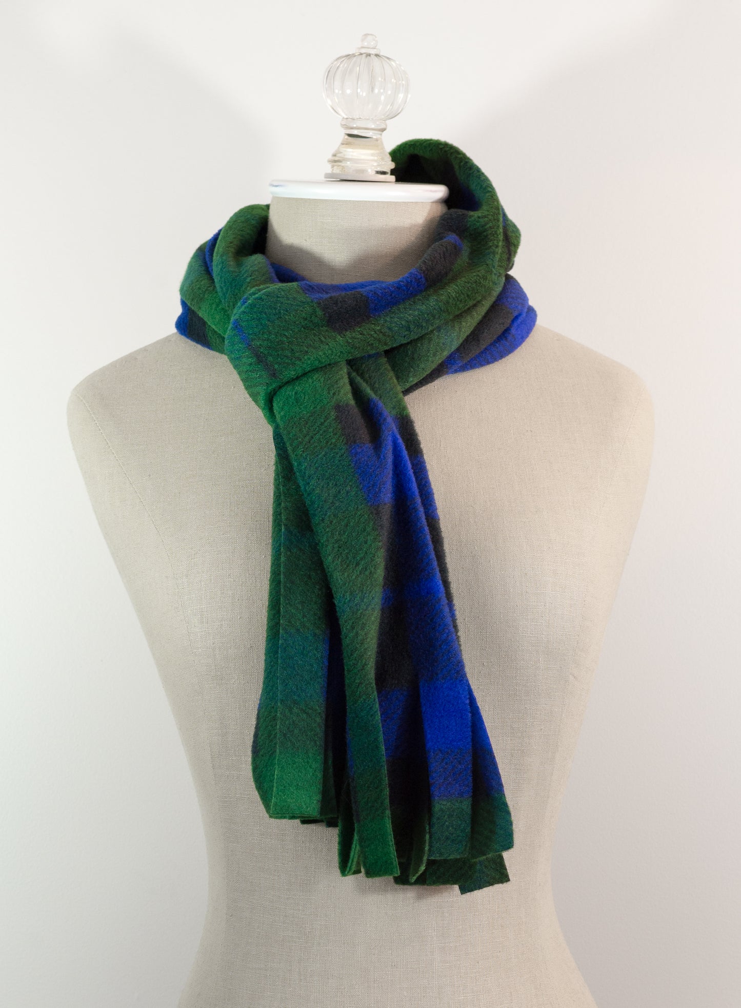 A tartan plaid scarf in green, blue, and black, draped on a white mannequin torso against a white background.
Photo by TheSurgeonsKnots.com [additional_image_link]