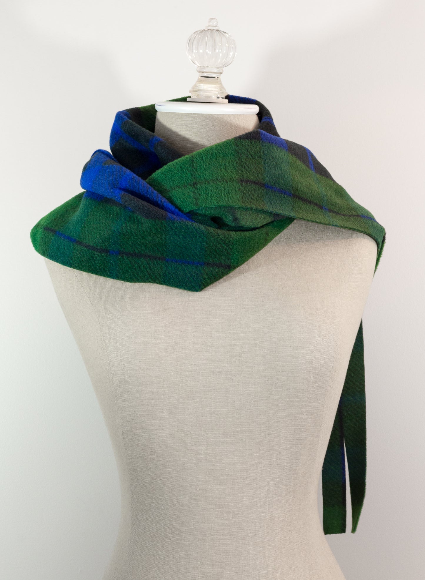 A tartan plaid scarf in green, blue, and black, draped on a white mannequin torso against a white background.
Photo by TheSurgeonsKnots.com [additional_image_link]