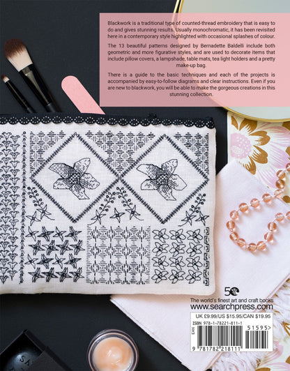 Back cover of a blackwork embroidery book, featuring a white embroidery sampler sheet with black stitched floral and geometric patterns, a pink text box with descriptive copy, a black thread spool, a pink fabric cutter, and a pearl necklace on a light background.
Photo by Search Press [additional_image_link]