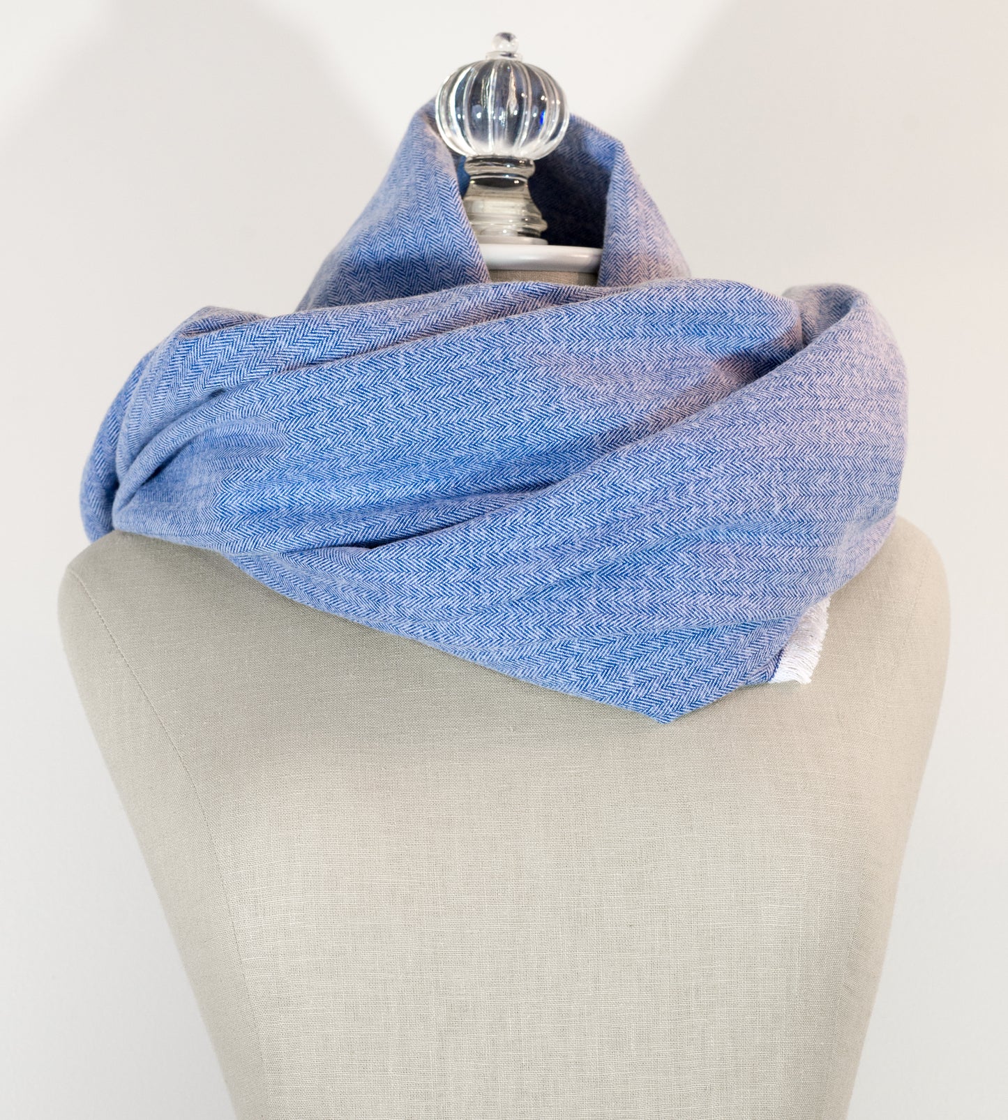 A blue herringbone flannel blanket scarf displayed on a mannequin, with the texture of the fabric visible. It has a fringe and appears to be a warm-colored accessory suitable for winter.
Photo by Karen King  [additional_image_link]