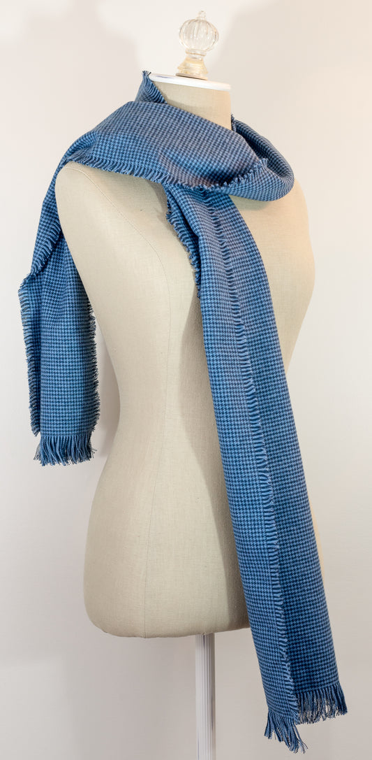 A blue houndstooth flannel scarf displayed on a mannequin, with the texture of the fabric visible. The scarf is frayed on all sides and has a fringe at the end.
Photo by Karen King [image_link]