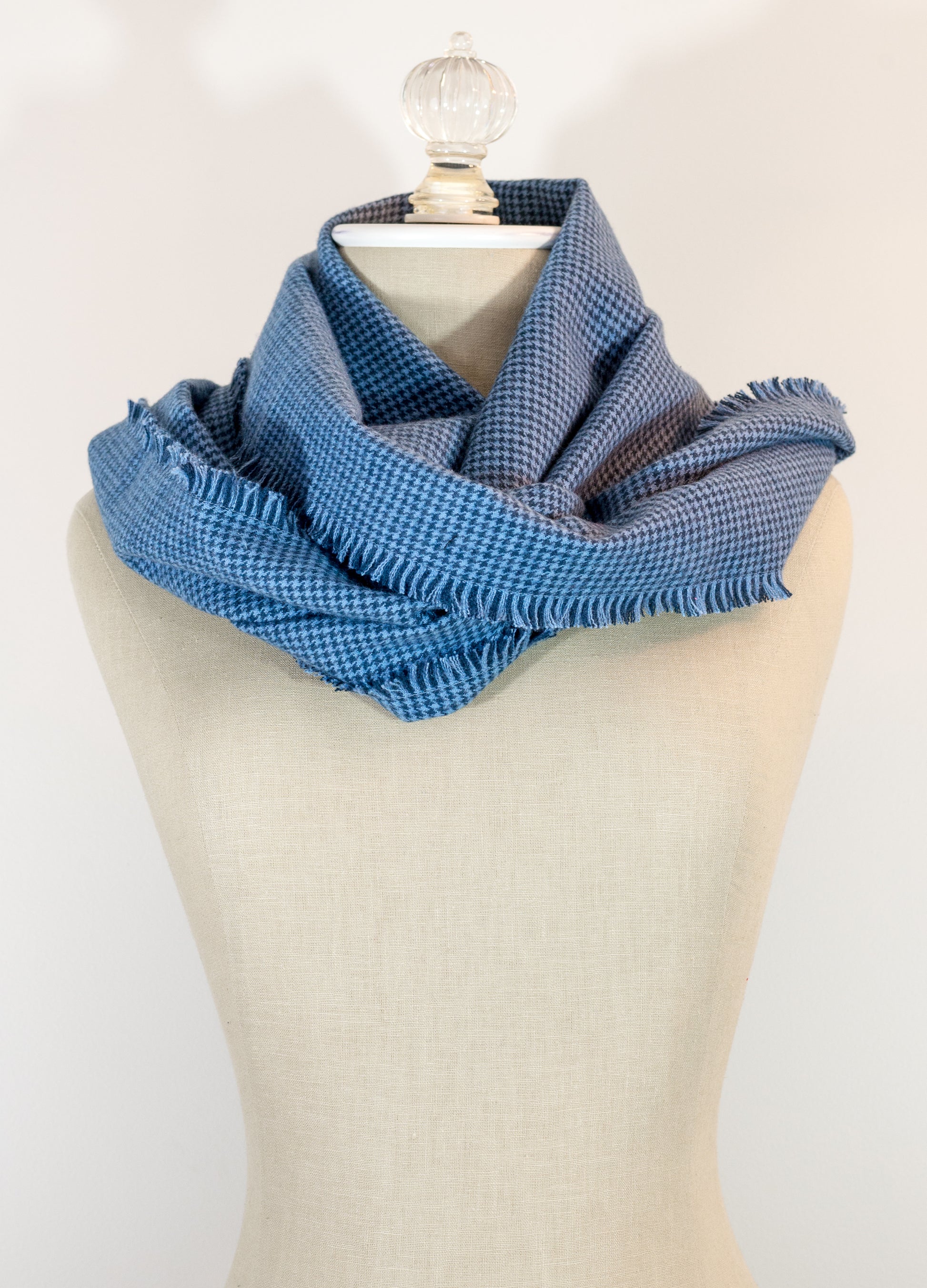 A blue houndstooth flannel scarf displayed on a mannequin, with the texture of the fabric visible. The scarf is frayed on all sides and has a fringe at the end.
Photo by Karen King [additional_image_link]