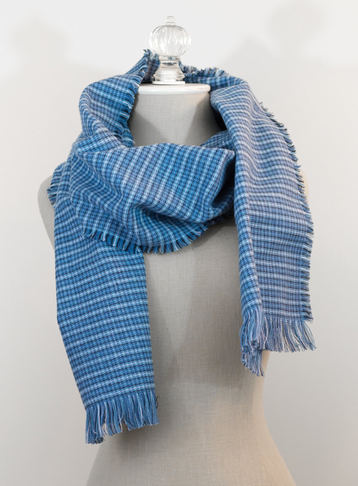 A blue tartan plaid flannel scarf displayed on a mannequin, with fringe detailing on the ends.
Photo by Karen King [image_link]