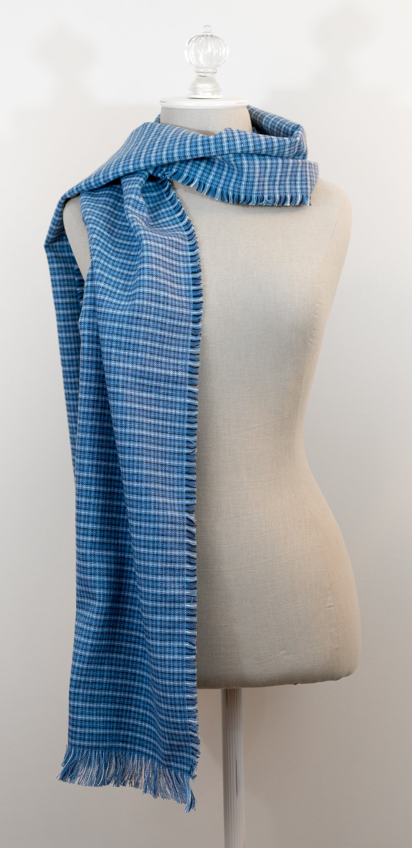 A blue tartan plaid flannel scarf displayed on a mannequin, with fringe detailing on the ends.
Photo by Karen King [additional_image_link]