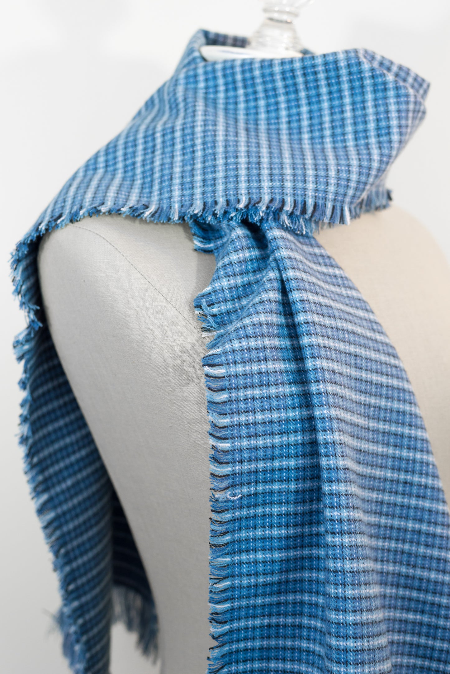A blue tartan plaid flannel scarf displayed on a mannequin, with fringe detailing on the ends.
Photo by Karen King [additional_image_link]