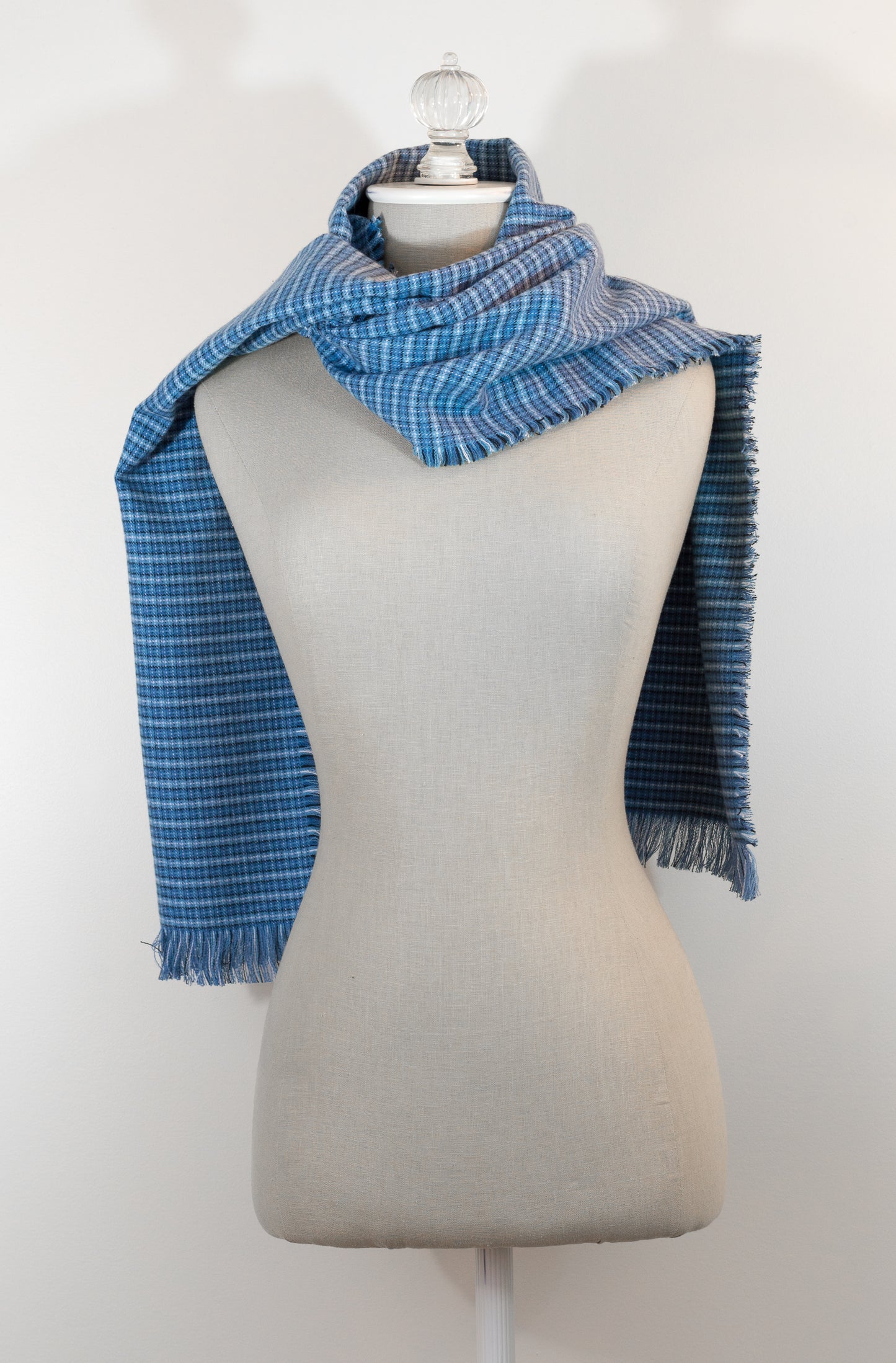 A blue tartan plaid flannel scarf displayed on a mannequin, with fringe detailing on the ends.
Photo by Karen King [additional_image_link]