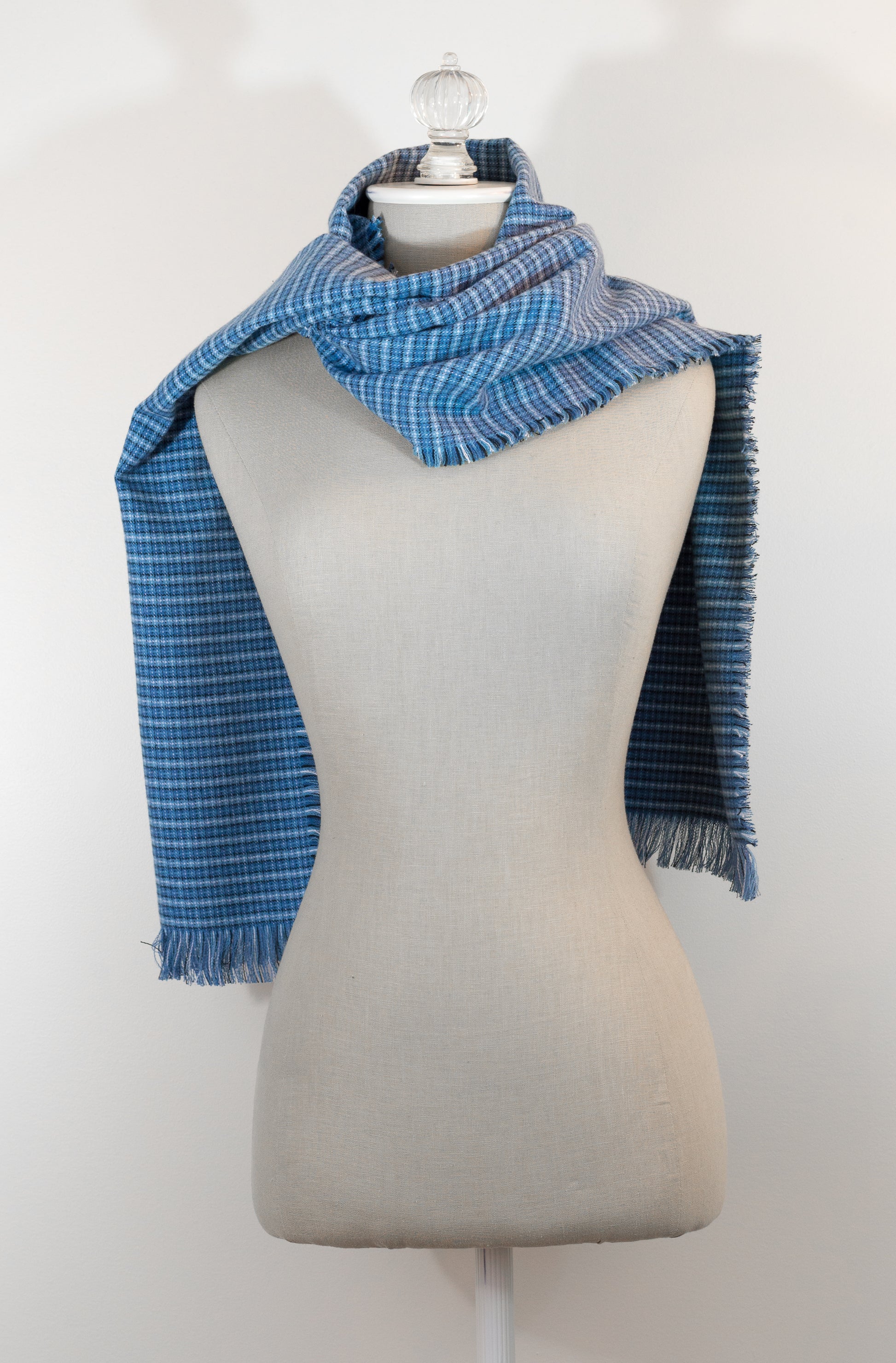 A blue tartan plaid flannel scarf displayed on a mannequin, with fringe detailing on the ends.
Photo by Karen King [additional_image_link]