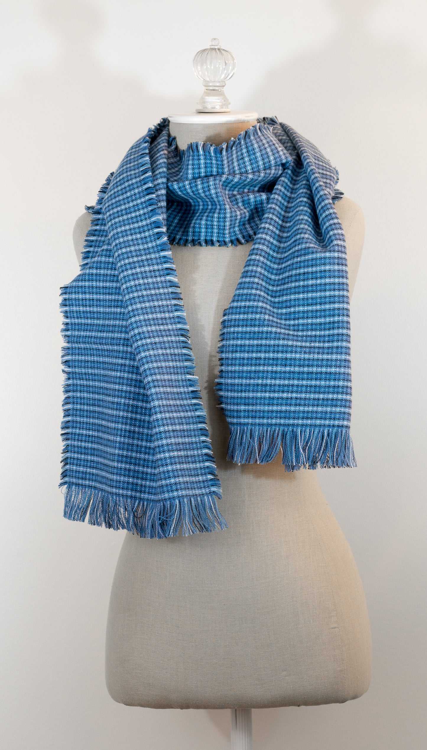 A blue tartan plaid flannel scarf displayed on a mannequin, with fringe detailing on the ends.
Photo by Karen King [additional_image_link]