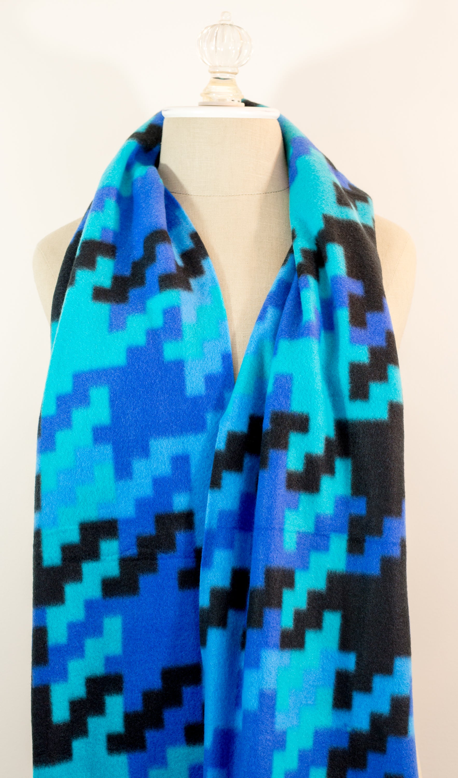 A scarf with a geometric houndstooth pattern in shades of blue and black, displayed on a mannequin.
Photo by Karen King [image_link]