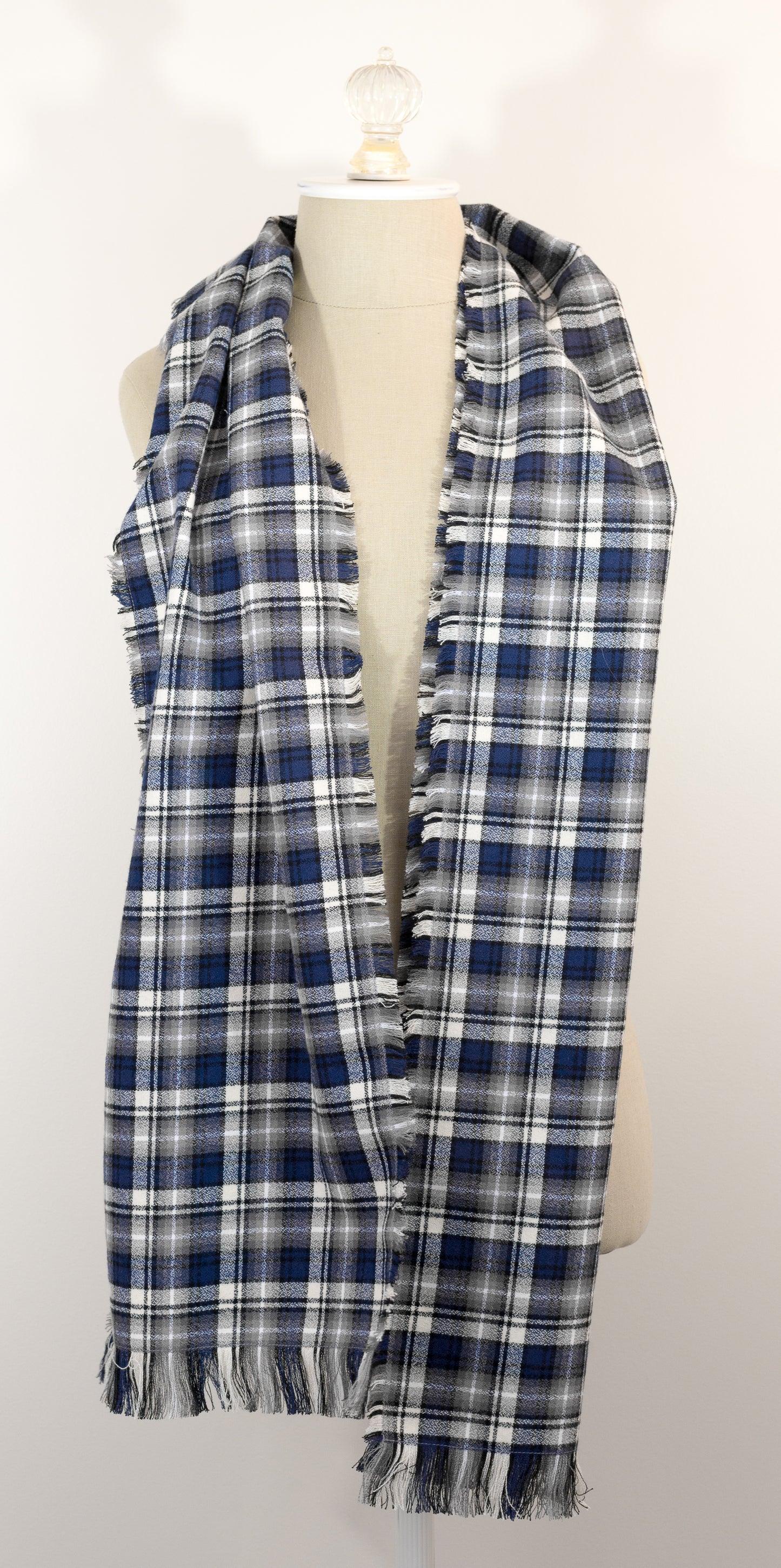 A navy blue, white, and gray plaid scarf with fringe details, draped on a cream-colored mannequin torso against a plain white background.
Photo by Karen King [additional_image_link]