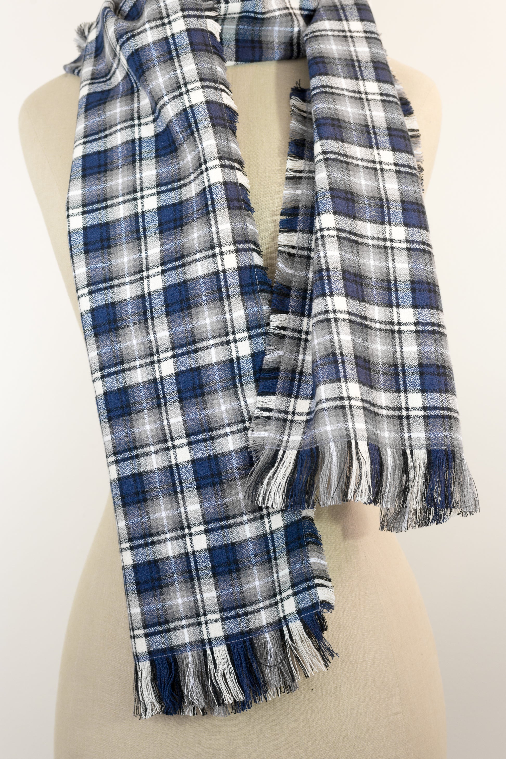A navy blue, white, and gray plaid scarf with fringe details, draped on a cream-colored mannequin torso against a plain white background.
Photo by Karen King [additional_image_link]