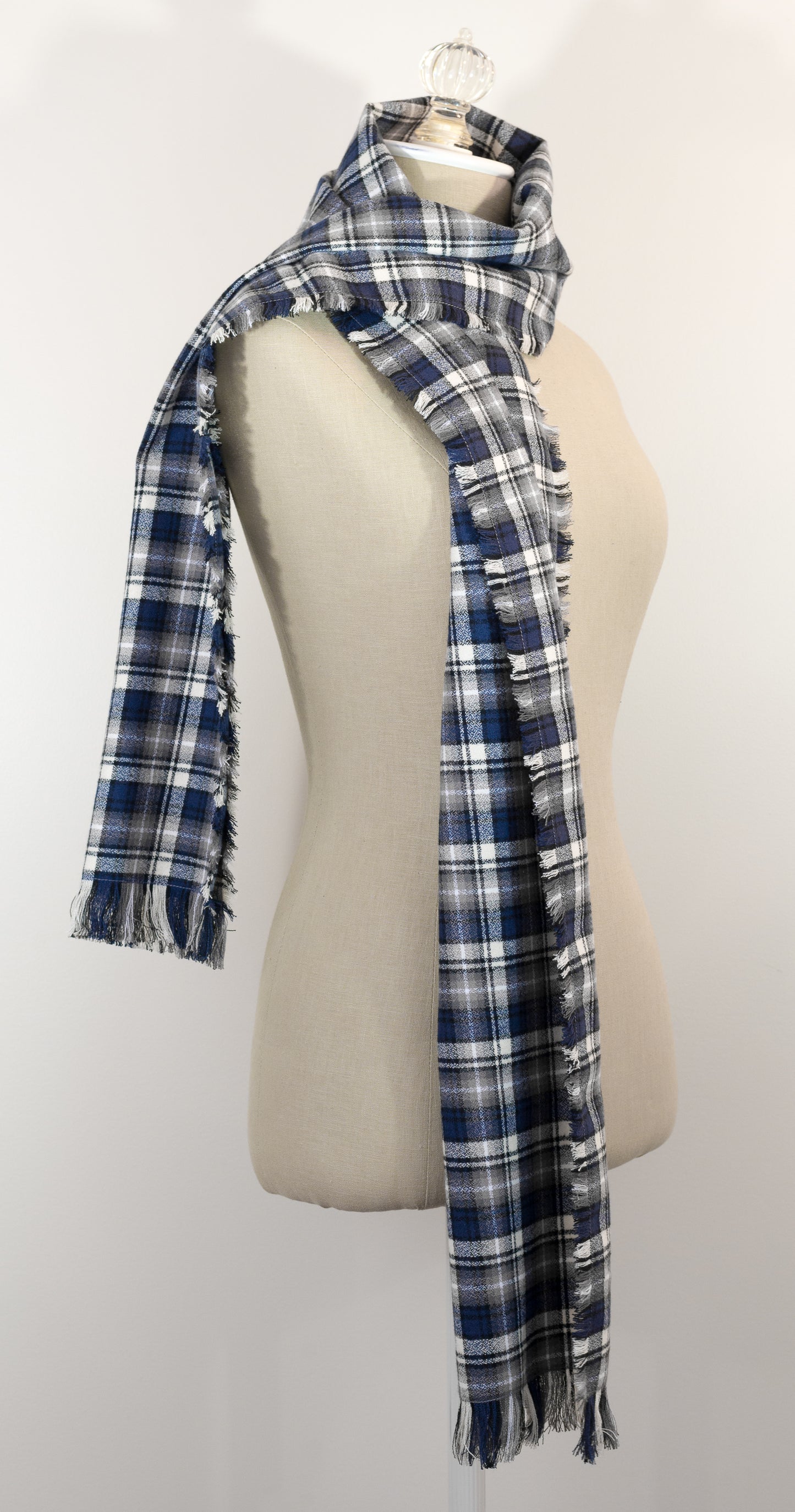 A navy blue, white, and gray plaid scarf with fringe details, draped on a cream-colored mannequin torso against a plain white background.
Photo by Karen King [additional_image_link]
