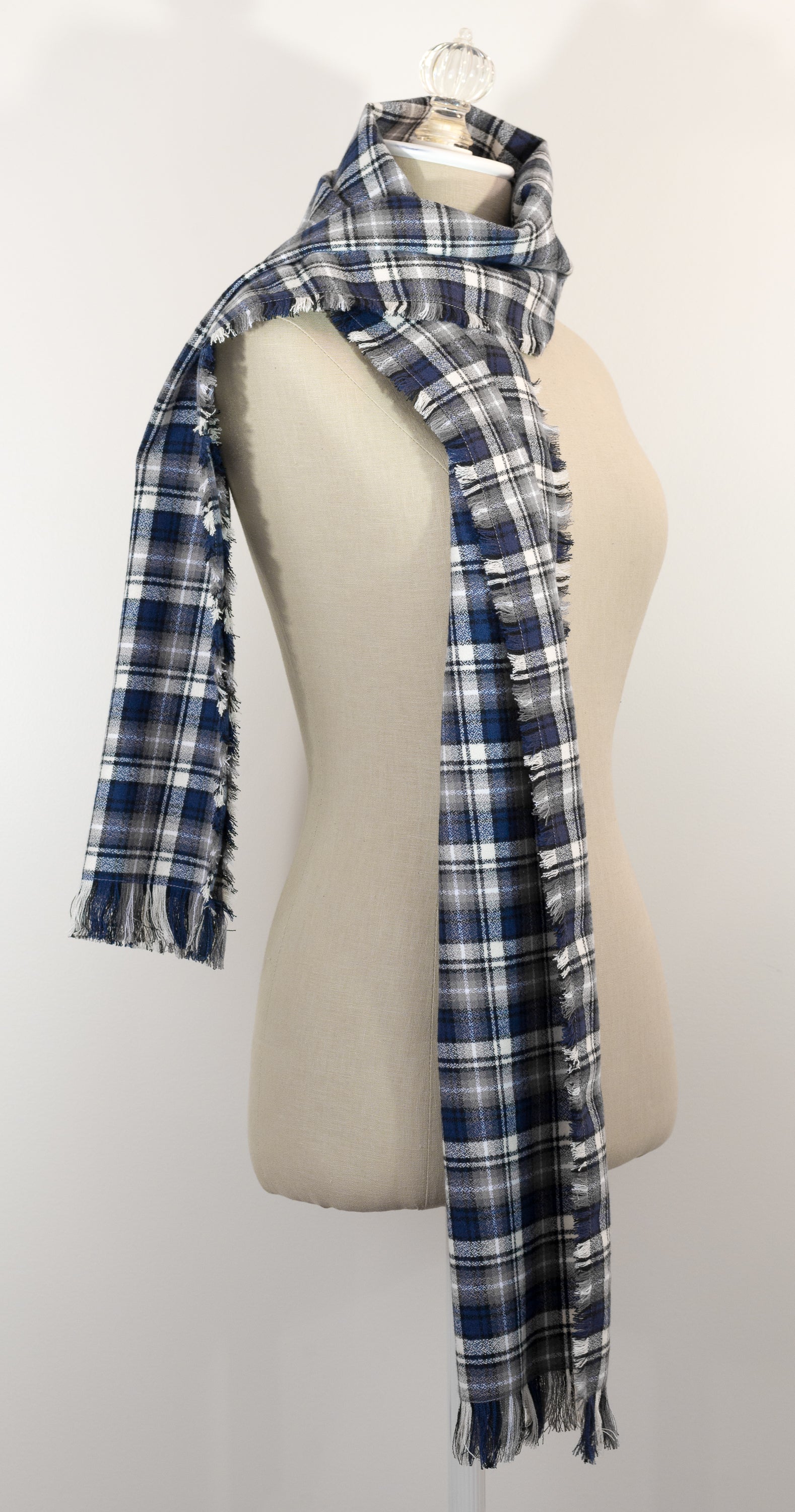 A navy blue, white, and gray plaid scarf with fringe details, draped on a cream-colored mannequin torso against a plain white background.
Photo by Karen King [additional_image_link]