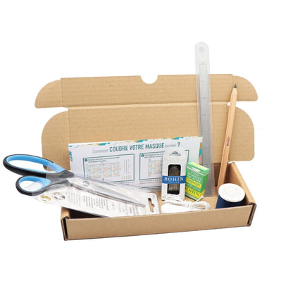 A cardboard craft kit box opened on a white background, containing a pair of blue-handled scissors, a clear ruler, a wooden pencil, printed instruction sheets, a small green box, a white container, and other small craft supplies.
Photo by Bohin [additional_image_link]