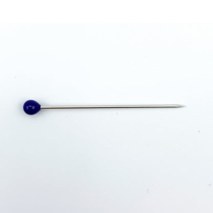 A long silver metal pin with a small, round, dark blue cabochon gemstone on one end, set against a plain white background.
Photo by Bohin [additional_image_link]