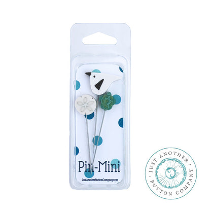 A pincushion kit packaging containing a wooden spool, a green felted wool ball, and a piece of silk ribbon, branded by Just Another Button Company.
Photo by JustAnotherButtonCompany.com [image_link]