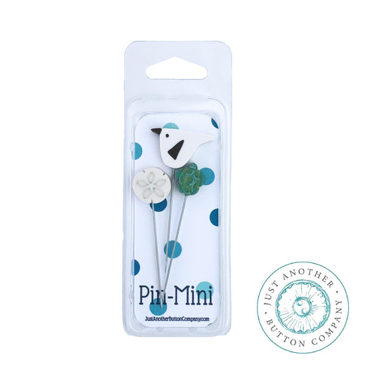 A pincushion kit packaging containing a wooden spool, a green felted wool ball, and a piece of silk ribbon, branded by Just Another Button Company.
Photo by JustAnotherButtonCompany.com [image_link]