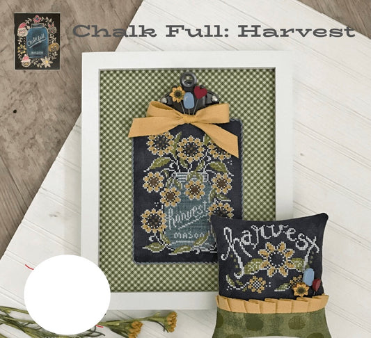 A framed cross-stitch or needlework sample titled 'Chalk Full: Harvest' is displayed on a white wooden surface with a rustic wood background. The artwork features a dark navy central panel with embroidered sunflowers, a blue mason jar, and a yellow ribbon bow, alongside a smaller matching pillow or cushion reading 'harvest' in white script.
Photo by HandsOnDesign.biz [image_link]