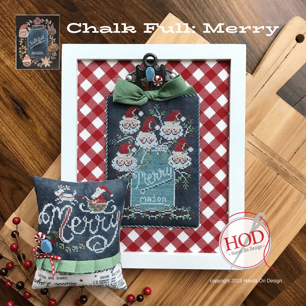 A framed and cushion-style Christmas cross-stitch design displayed on a wooden surface, with a red-and-white gingham backing, a green bow, Santa motifs, and the text 'Chalk Full: Merry' and 'Hand On Design' visible.
Photo by HandsOnDesign.biz [image_link]