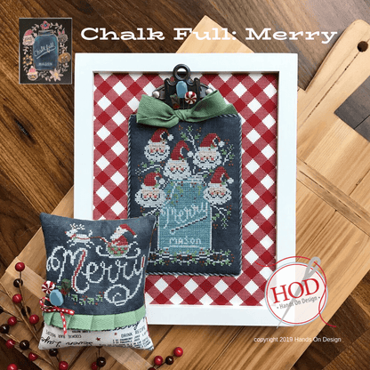 A framed and cushion-style Christmas cross-stitch design displayed on a wooden surface, with a red-and-white gingham backing, a green bow, Santa motifs, and the text 'Chalk Full: Merry' and 'Hand On Design' visible.
Photo by HandsOnDesign.biz [image_link]