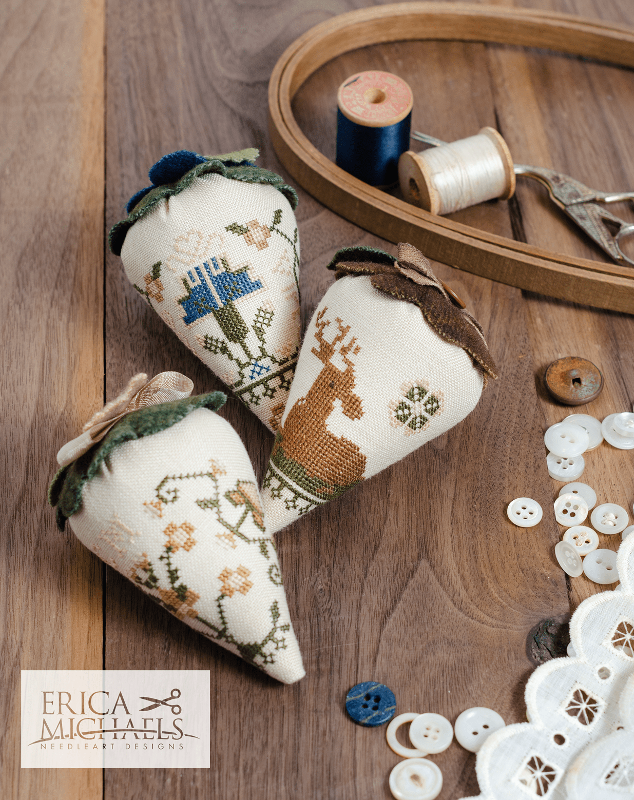 Three linen cross stitch pincushions with floral embroidery designs, accompanied by a spool of linen thread, a needle, and buttons.
Photos by Erica Michaels [image_link]