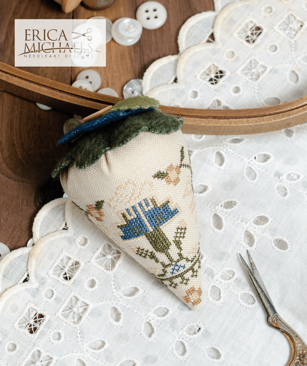 One linen cross stitch pincushions with floral embroidery designs, accompanied by a spool of linen thread, a needle, and buttons.
Photos by Erica Michaels [additional_image_link]