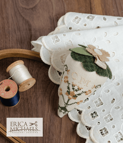 One linen cross stitch pincushions with floral embroidery designs, accompanied by a spool of linen thread, a needle, and buttons.
Photos by Erica Michaels [additional_image_link]