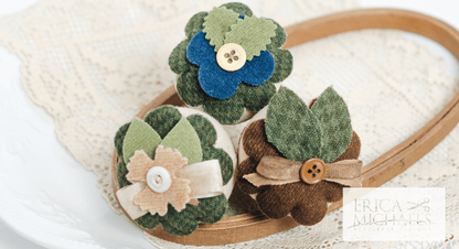 Three linen cross stitch pincushions with floral embroidery designs, accompanied by a spool of linen thread, a needle, and buttons. View from the top with embellishments.
Photos by Erica Michaels [additional_image_link]