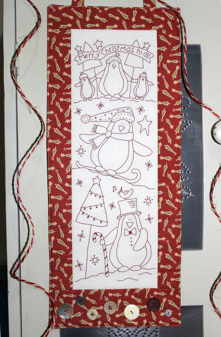 A vertical Christmas penguin-themed fabric hanging or banner with a red patterned border, a white center panel, and black line drawings of penguins, a Christmas tree, candy canes, and the text 'Merry Christmas to all.'.
Photo by The Birdhouse Patchwork Designs [image_link]