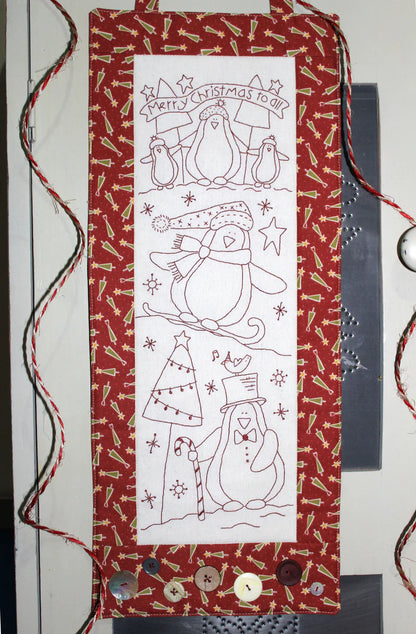 A vertical Christmas penguin-themed fabric hanging or banner with a red patterned border, a white center panel, and black line drawings of penguins, a Christmas tree, candy canes, and the text 'Merry Christmas to all.'.
Photo by The Birdhouse Patchwork Designs [image_link]