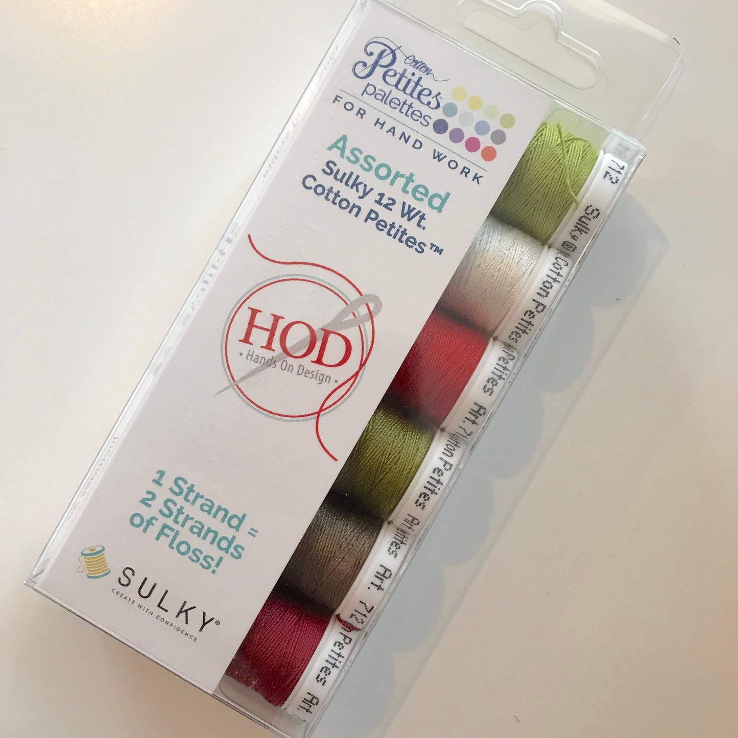 A package of HOD Sutly 13 wt Cotton Petite assorted thread spools in a clear plastic case with a white printed insert. The visible thread colors include olive green, light pink, red, brown, and dark gray.
Photo by HandsOnDesign.biz [additional_image_link]