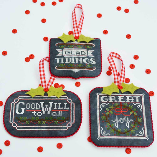 Three cross-stitched Christmas ornaments 'Glad Tidings' Goodwill to all' and ' Great joy' with festive sayings on a white background with red berries.
Photo by HandsOnDesign.biz [image_link]