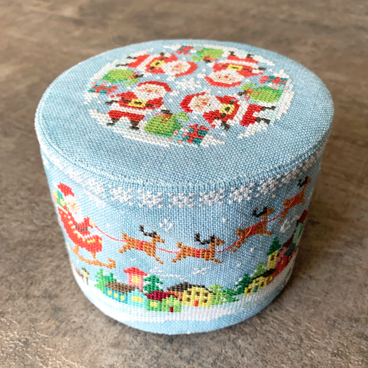 A round, light blue needlepoint canvas featuring a festive Christmas design with Santa Claus, reindeer, snowflakes, and a small village scene.
Photo by Tiny Modernist [image_link]