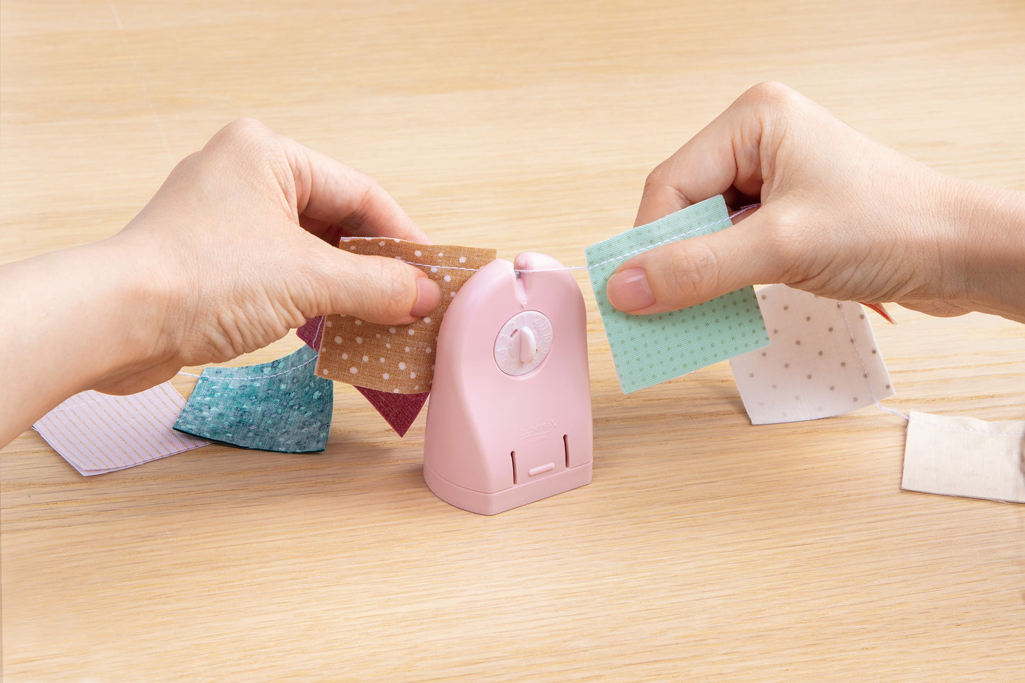 Pink adhesive bandage dispenser with hands applying bandages on a wooden surface.
Photo by Clover-USA.com [additional_image_link]